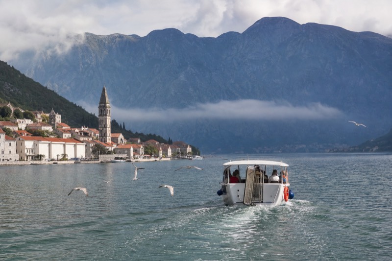 Morning mist lifting off the fjord-like Bay of Kotor, reached on a day trip from Dubrovnik in Croatia, a small tour boat crosses toward Venetian campaniles below black mountains