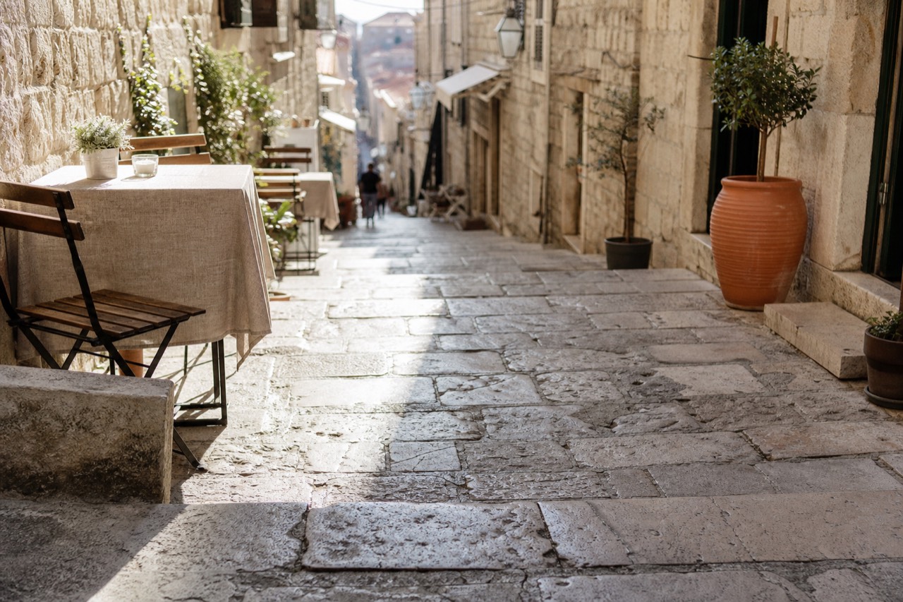 A stone street in Dubrovnik Old Town with cafe tables and shopfronts in morning light