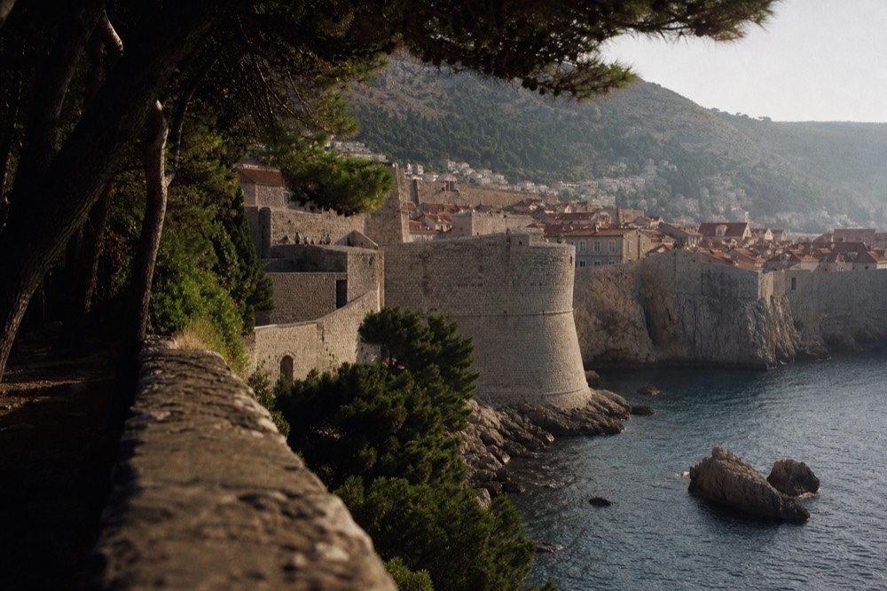 Stone city walls of Dubrovnik rising above the sea with red roofs behind them