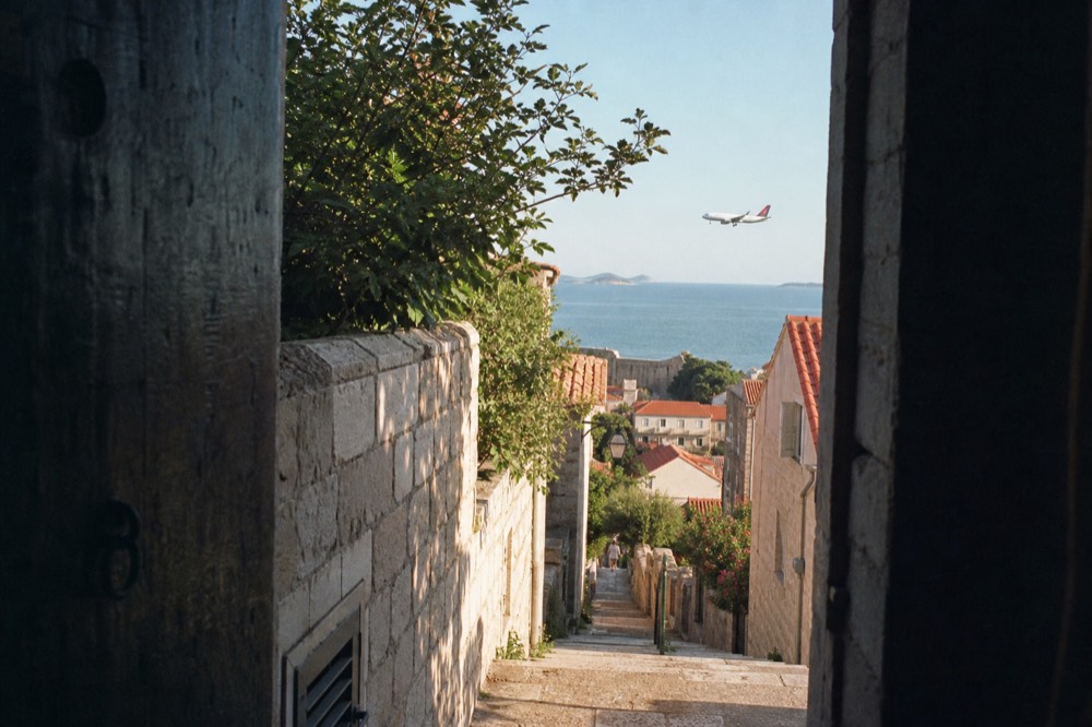 A plane descending over the Adriatic coastline toward Dubrovnik with red rooftops in the distance