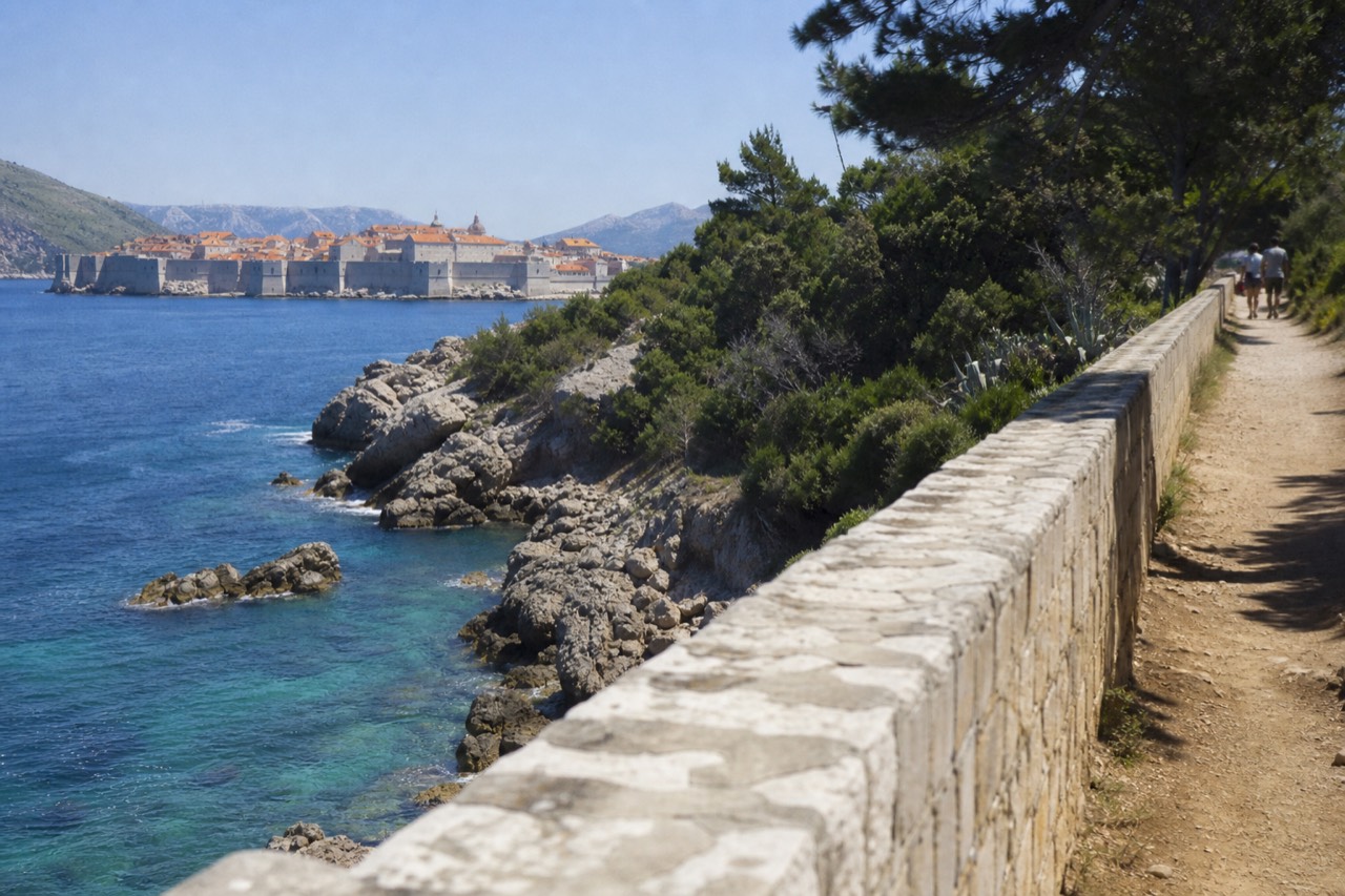 Rocky shoreline of a green island with clear turquoise water and the walled city across the bay