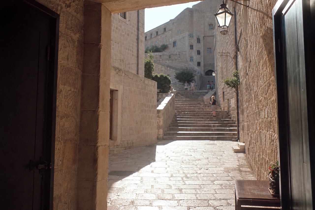 Sunlit limestone street inside Dubrovnik Old Town with stone staircases rising toward the city walls
