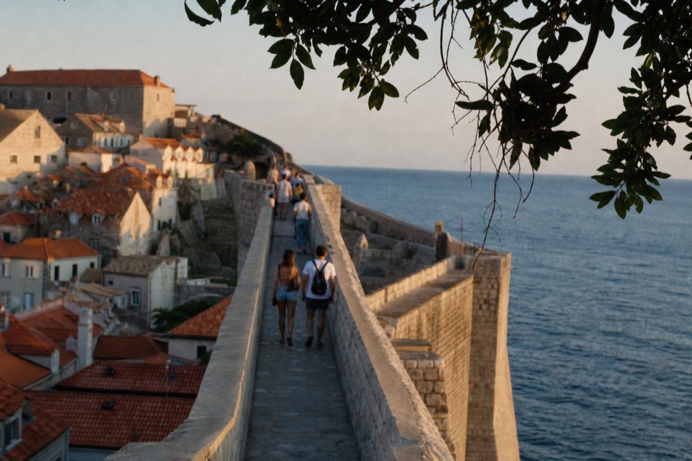Walkers on a stone wall path above tiled rooftops of the old town