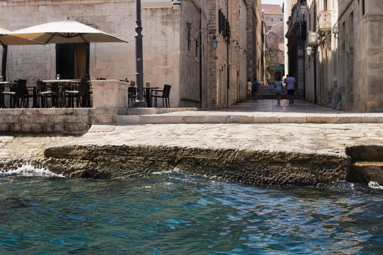 A stone alley terrace with cafe tables and chairs beside a lamplit Dubrovnik street