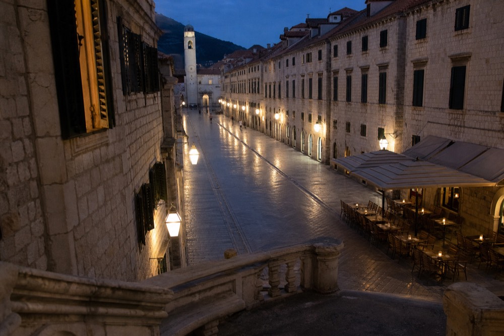 Stradun street lit by lamps at dusk with empty tables outside a restaurant