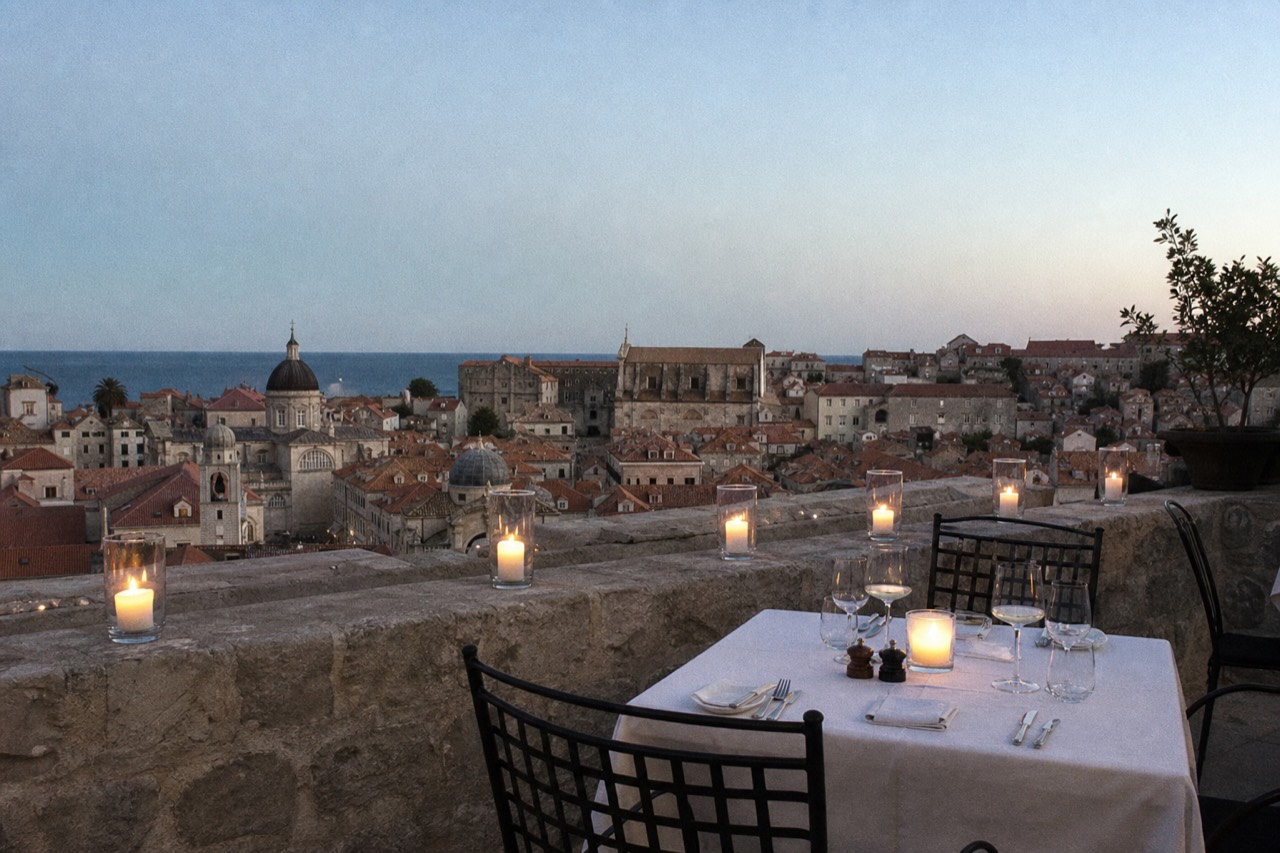 A candlelit restaurant terrace table above the tiled roofs of Dubrovnik Old Town at dusk