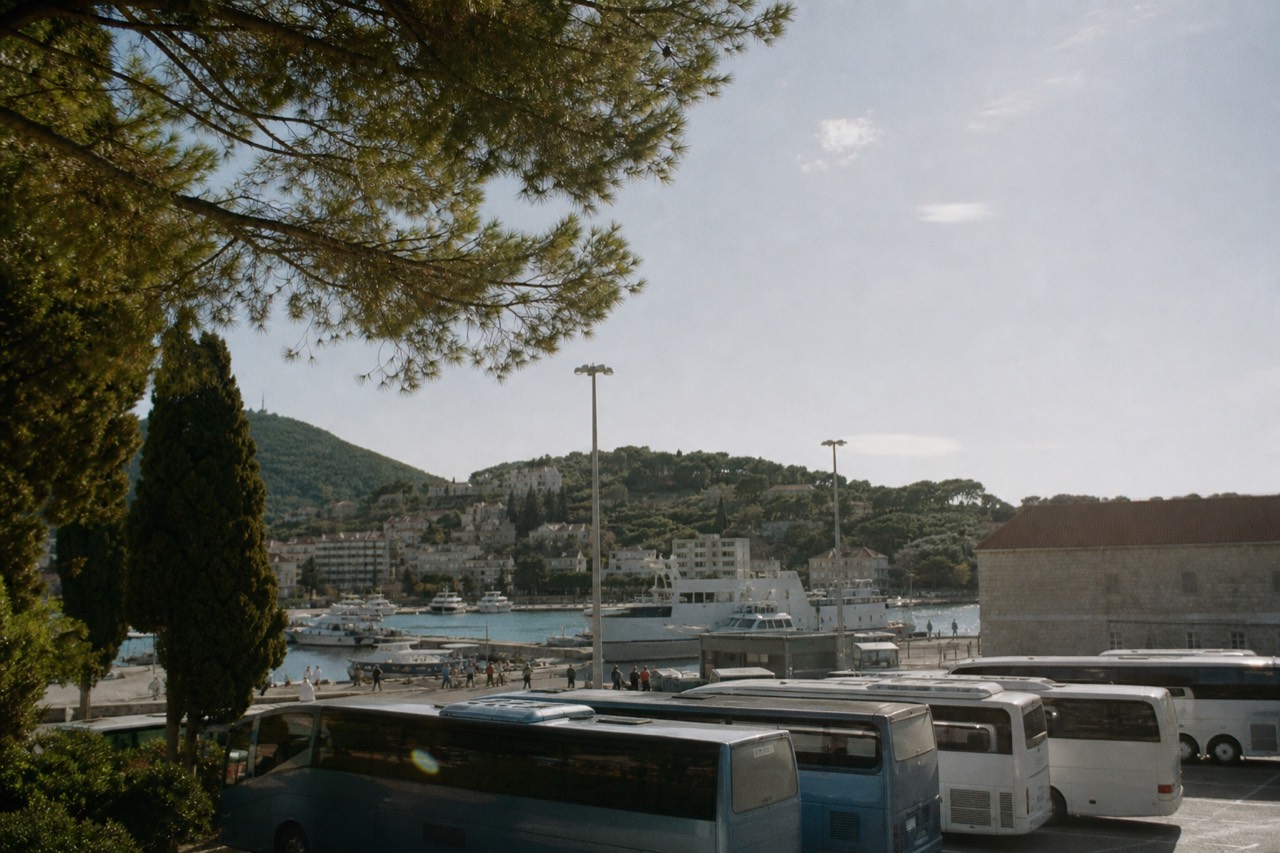 Buses parked at the Gruž terminal with boats moored in the harbour behind them