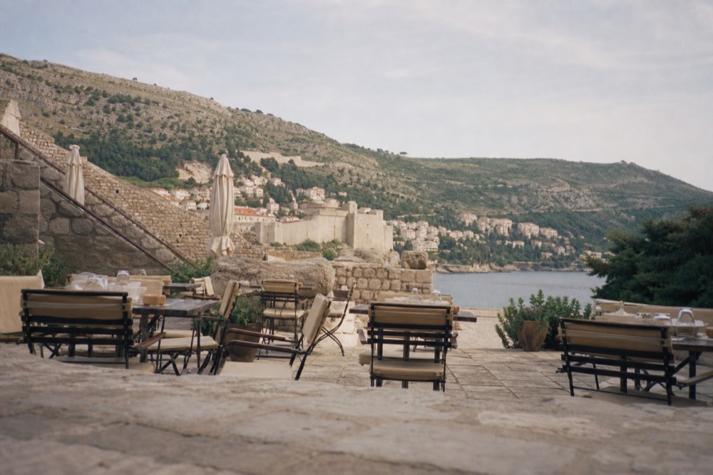 A café terrace on a stone plaza in Dubrovnik with morning light on the tables