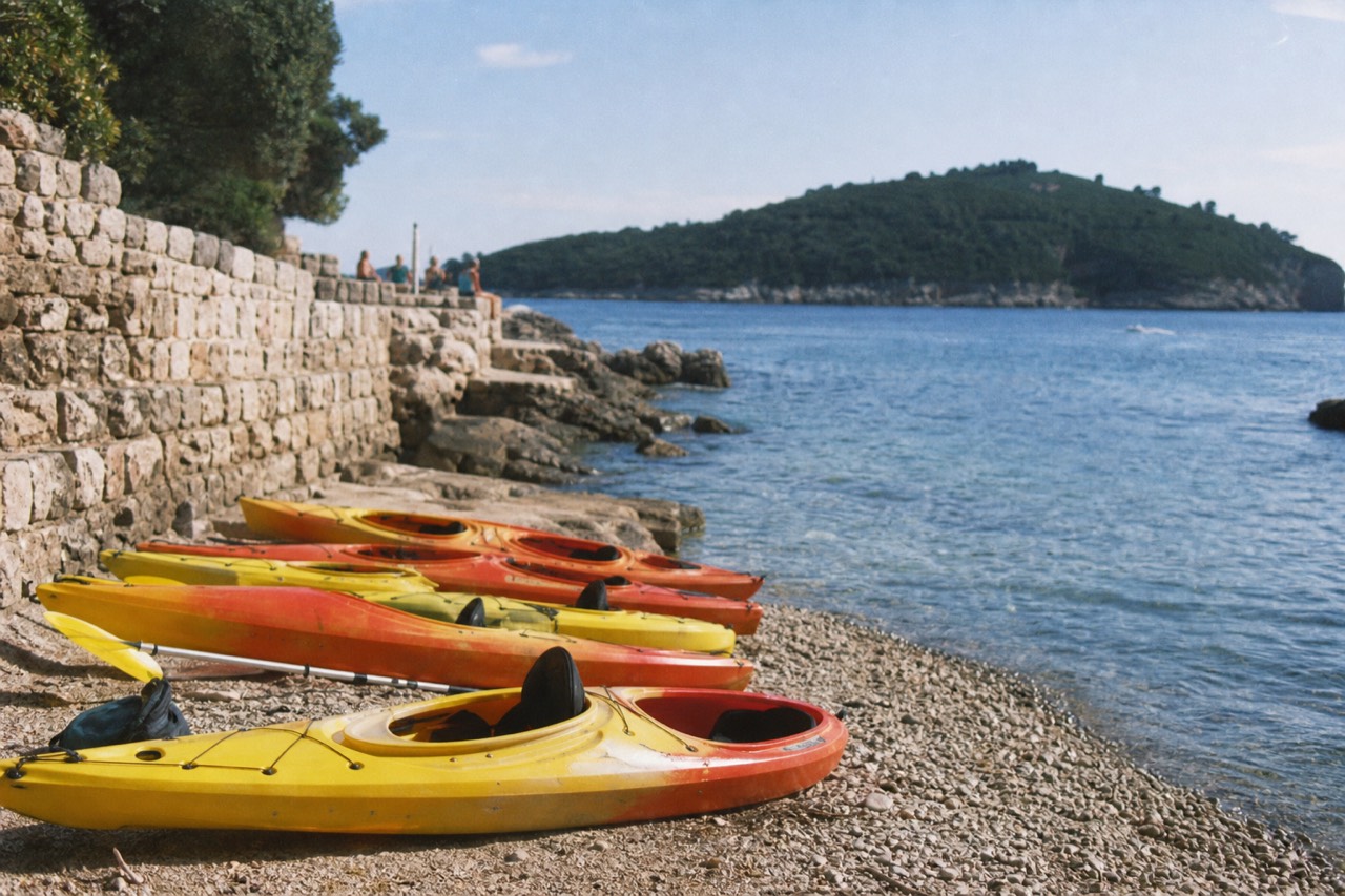 Kayaks resting on a rocky shore with Lokrum island and the Adriatic sea in the background