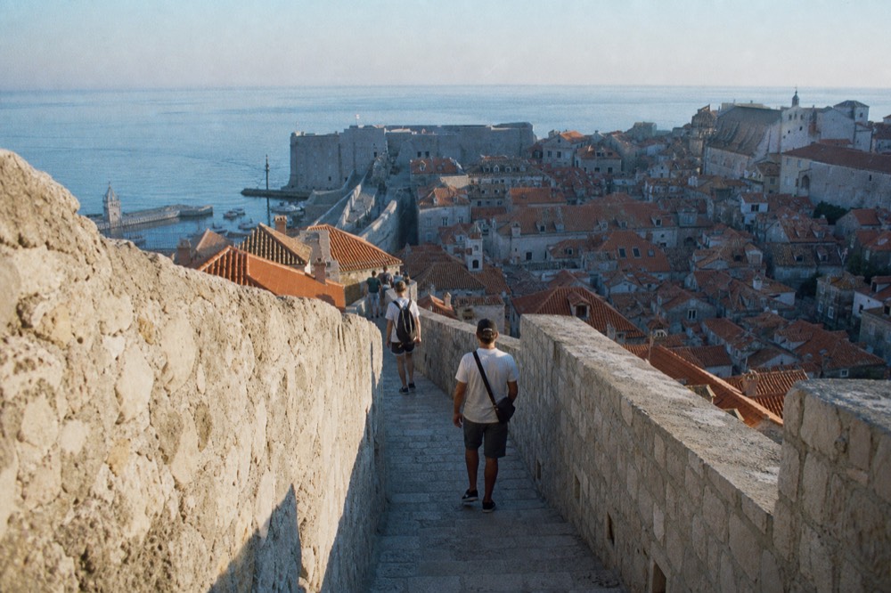 Walkers on the stone wall path high above the tiled roofs of the old town