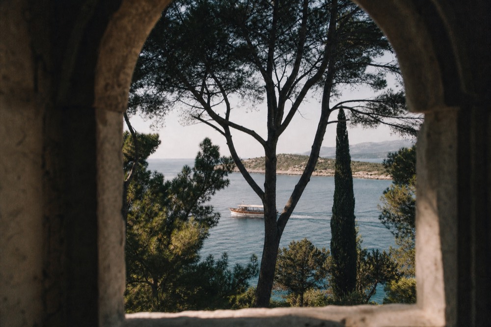 A wooden tourist boat cruising along a coastline of low hills and clear water