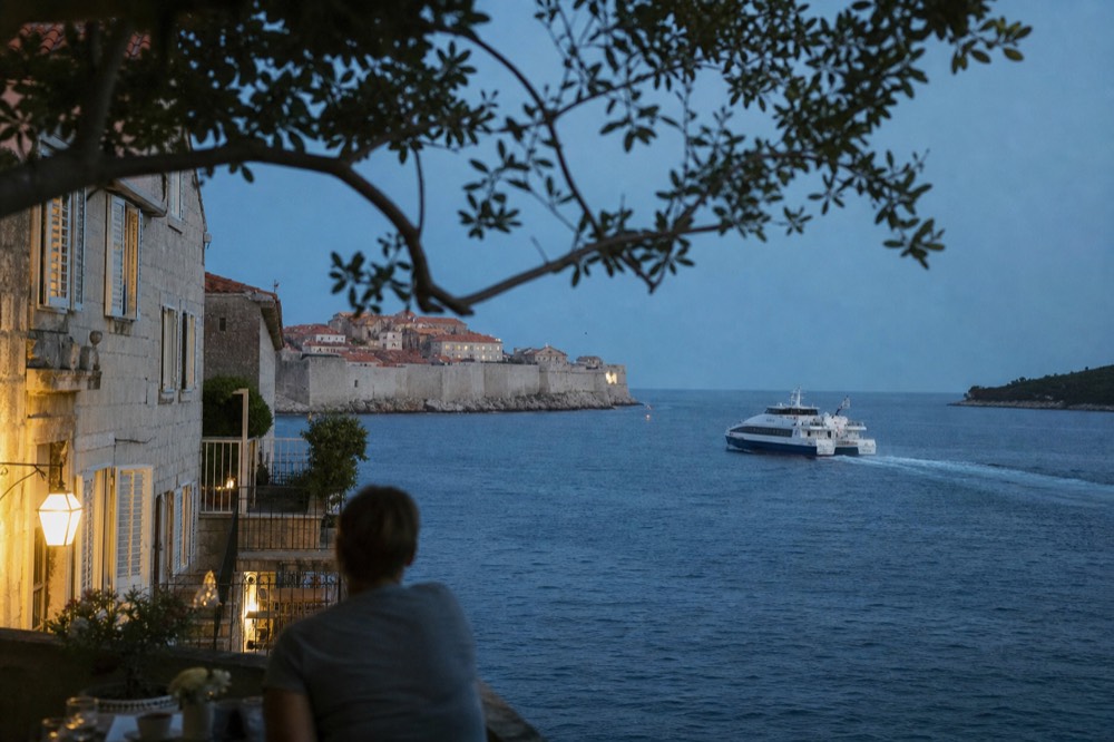 A catamaran ferry cutting across blue Adriatic water toward a walled island town