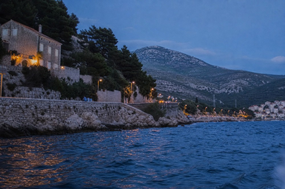 A coastal road curving along a blue bay with steep hillsides on one side