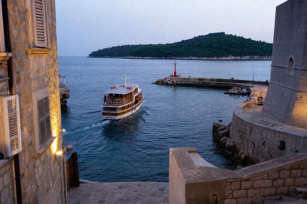 A wooden passenger boat departing the Old City Harbour toward the green island of Lokrum