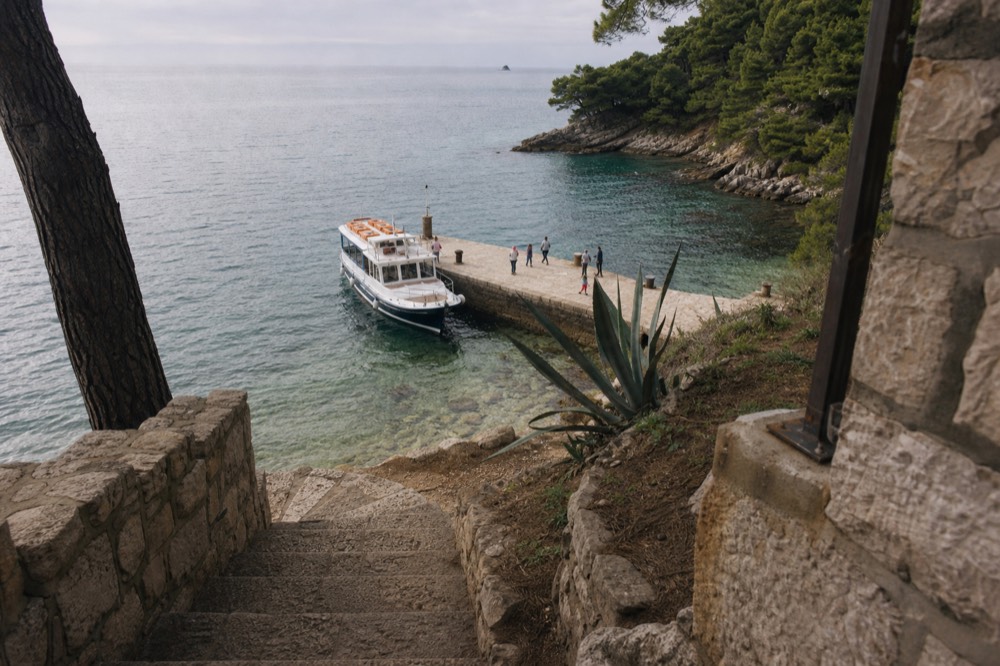 A stone pier on Lokrum with a small passenger boat moored beside clear green water