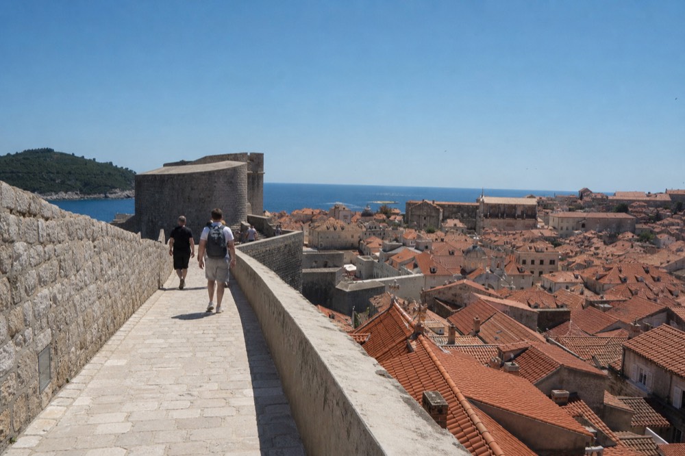 Walkers on the stone wall path above Dubrovnik's red rooftops