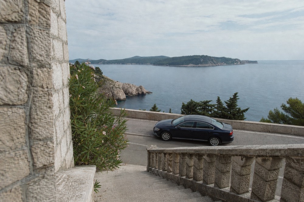 A sedan parked on a coastal viewpoint road above blue Adriatic water
