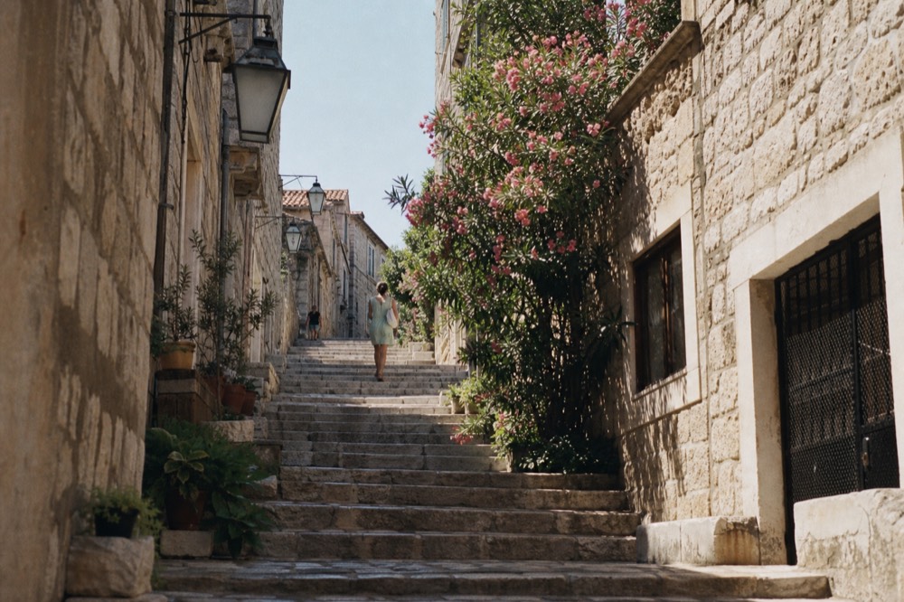 Sunlit limestone street in Dubrovnik Old Town with stone staircases climbing between buildings