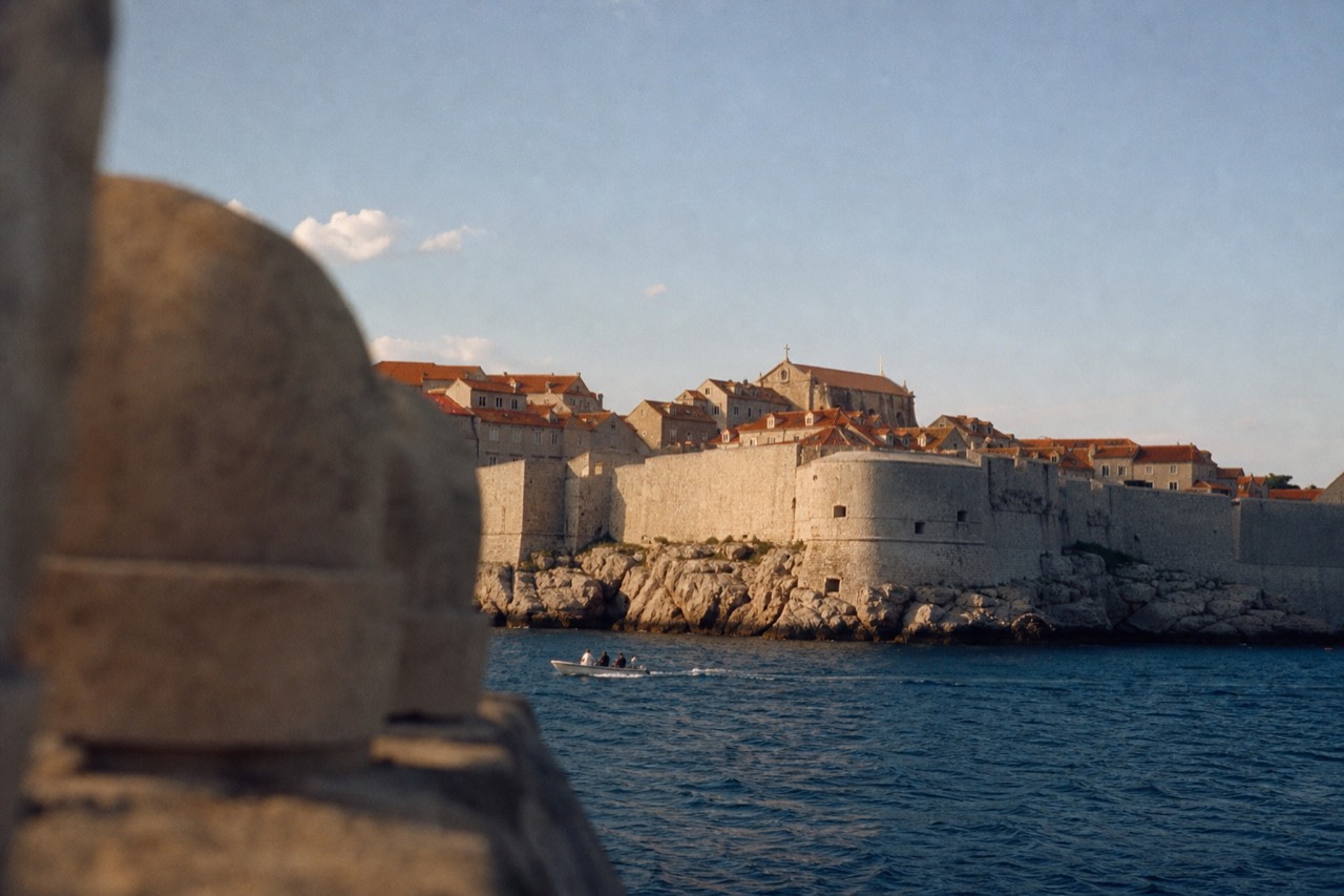 The walled Old Town of Dubrovnik seen from the sea at midday, terracotta roofs inside the stone walls