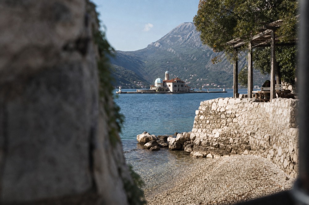 A stone church on a small island in the Bay of Kotor with mountains behind it