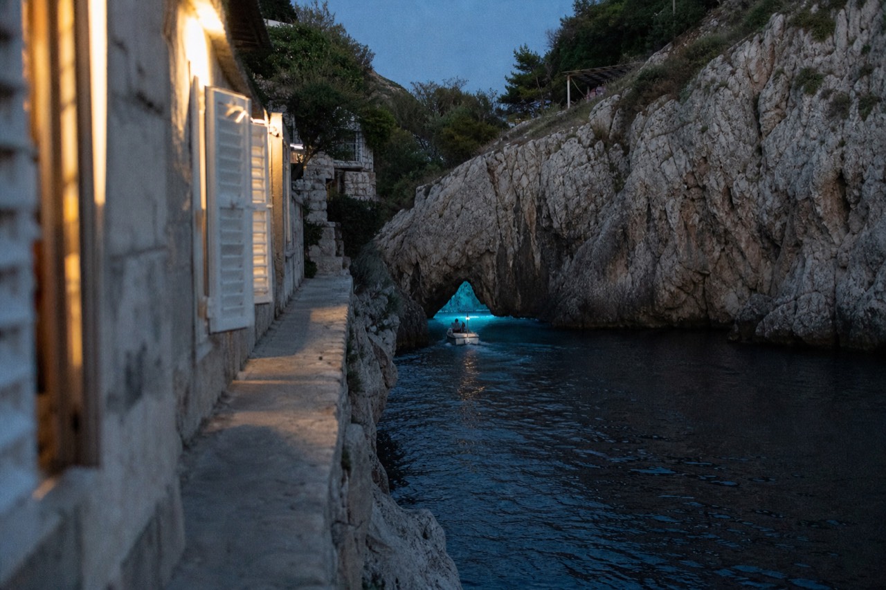 A small boat entering a glowing blue sea cave between pale limestone cliffs