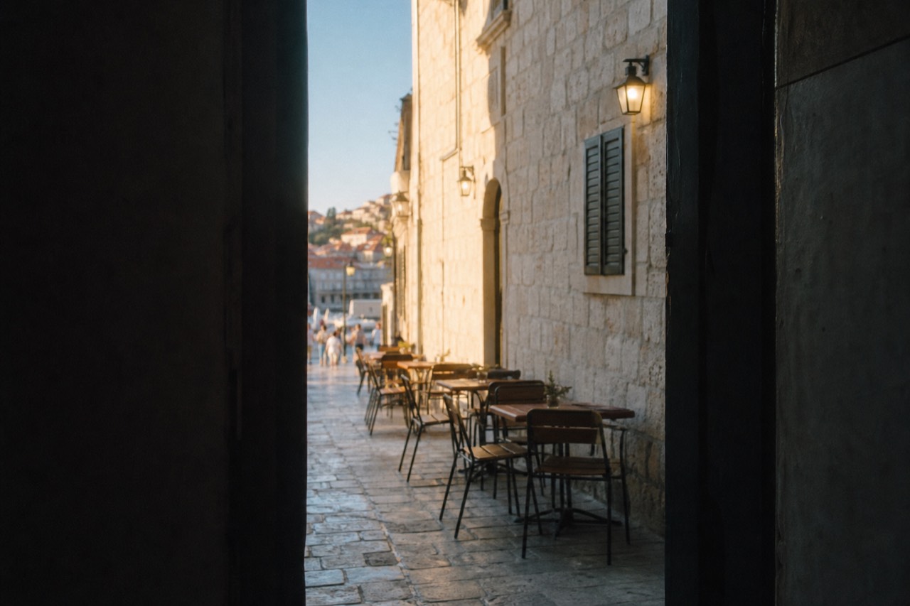 Sunlit limestone street in Dubrovnik Old Town with cafe tables along the wall