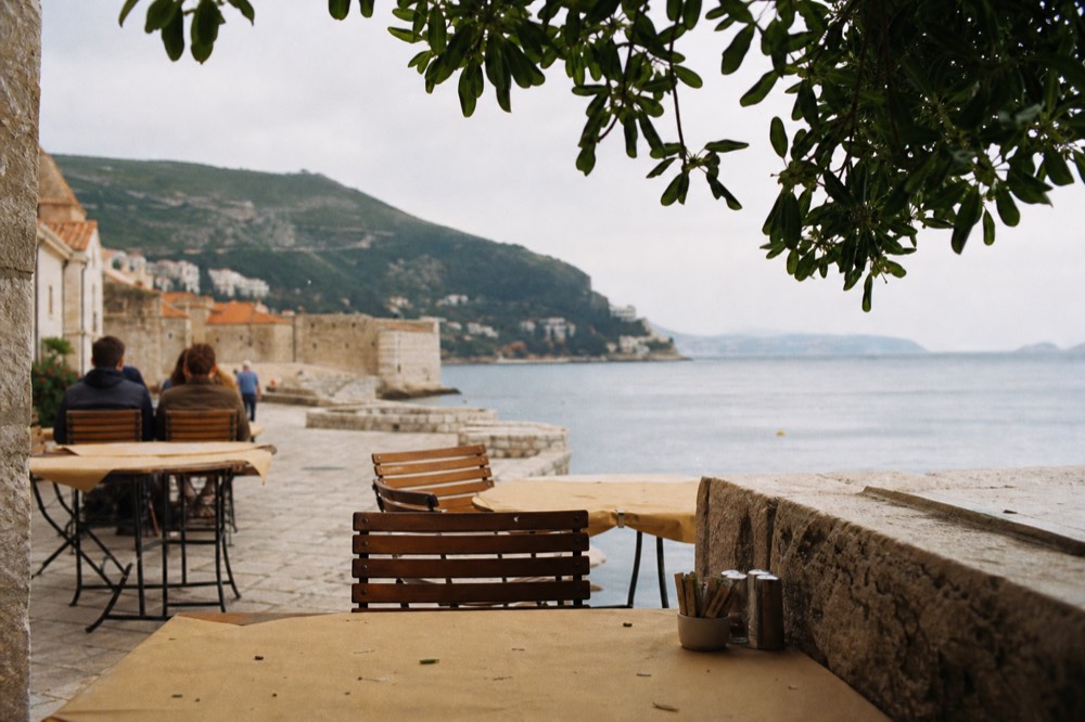 A cafe terrace on a stone square in Dubrovnik with paper tablecloths and morning light