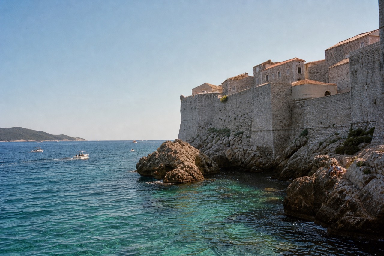 A rocky Adriatic shoreline below stone walls with clear turquoise water