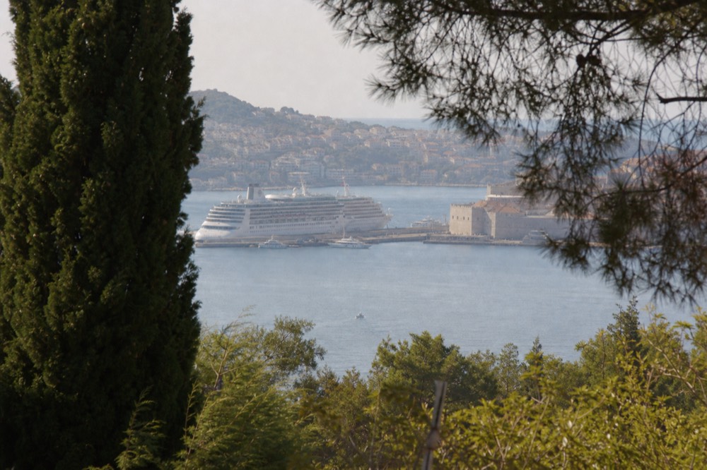 A wide bay with a cruise ship at a dock and a historic walled town across the water
