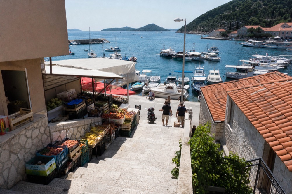 Market stalls with crates of fruit beside a harbour with small boats