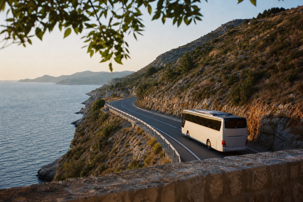 A modern coach driving along a coastal highway with the Adriatic Sea on one side and rocky hills on the other