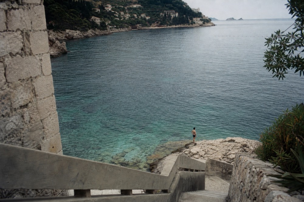 Rocky shoreline with clear shallow water and a swimmer standing on smooth limestone