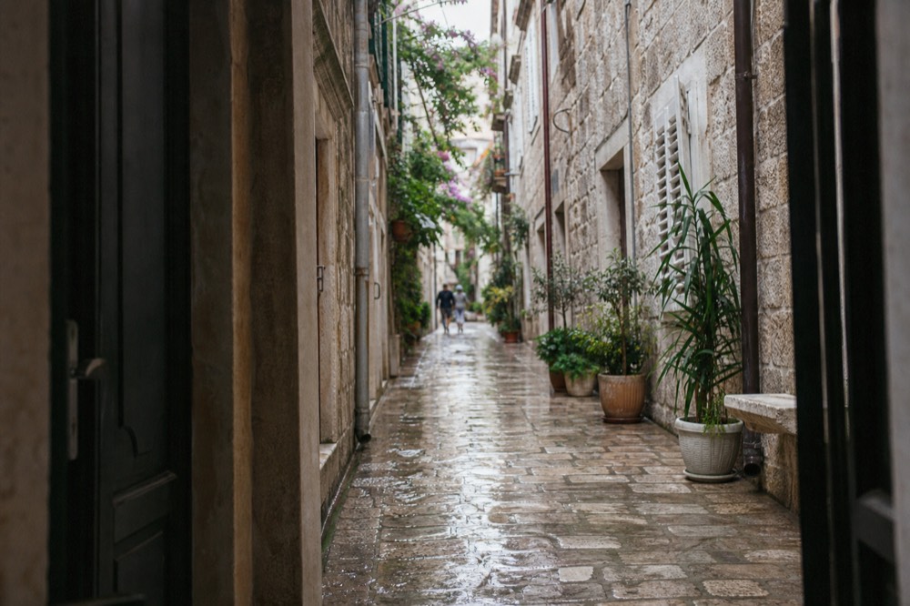 Narrow stone lane in Korcula old town with shuttered windows and potted plants