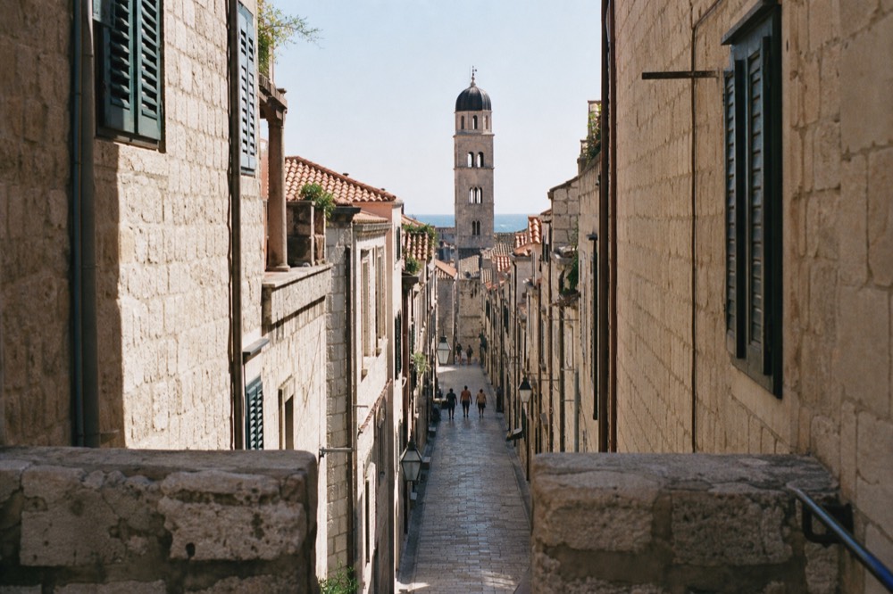 A flat limestone street lined with stone buildings leading toward a bell tower