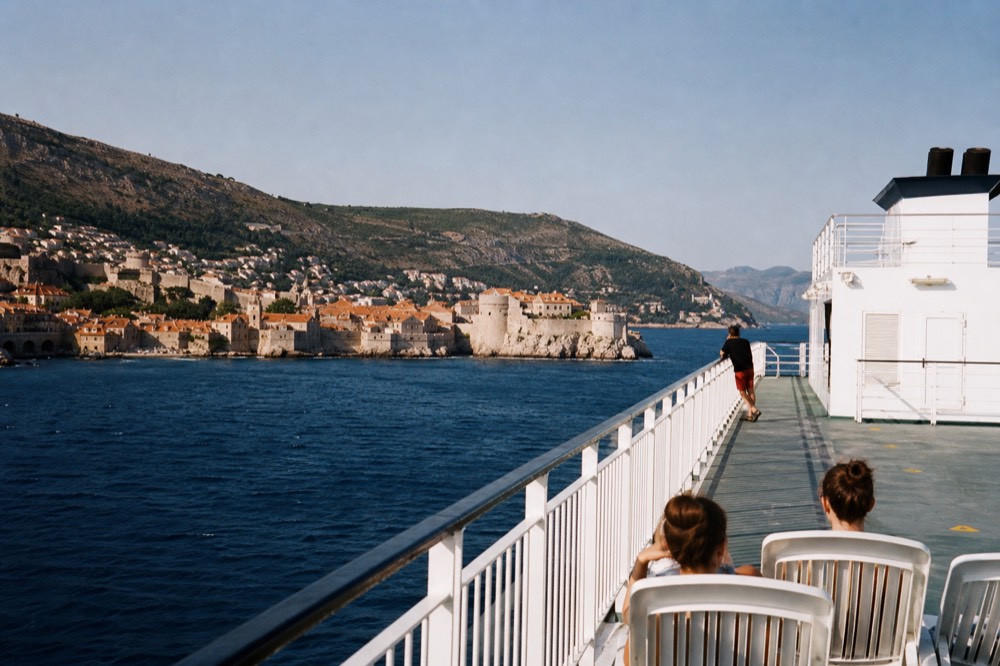 A car ferry deck with railings and island hills in the background under a clear sky