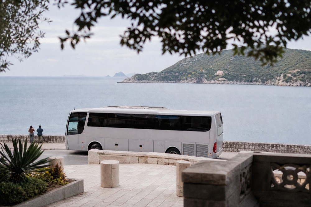 A long-distance coach parked at a coastal stop with the Adriatic sea behind it