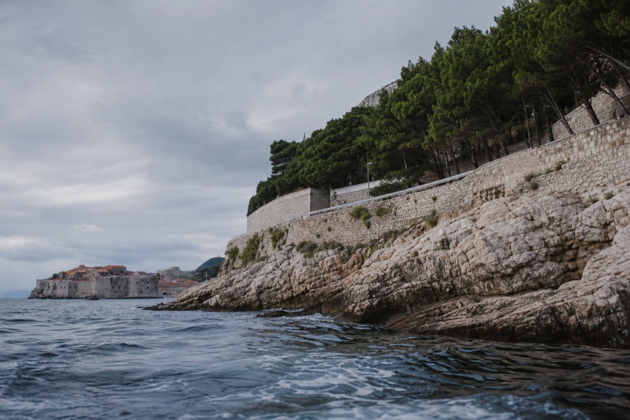 A coastal road curving above the Adriatic with the walled old town of Dubrovnik in the distance