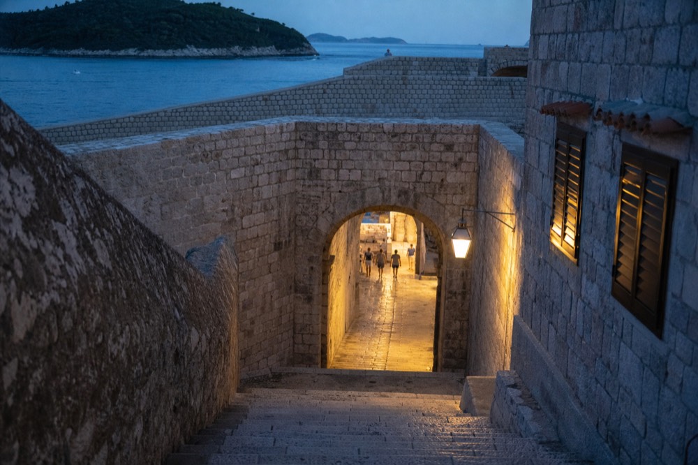 A stone gate and fortified wall of Dubrovnik's old city with sunlight on the limestone paving