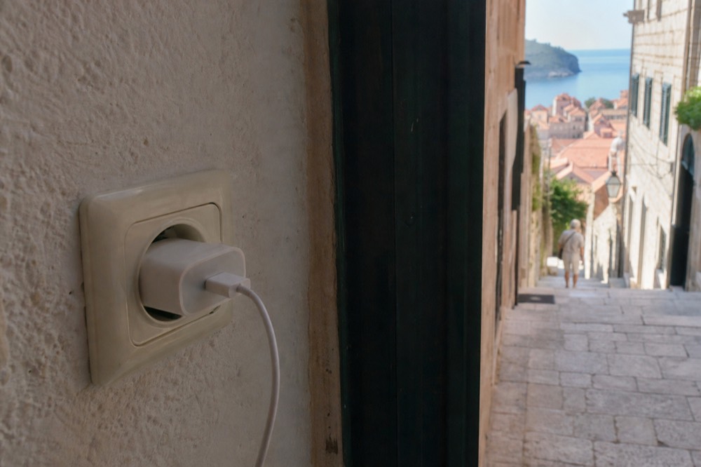 A close-up of a European wall socket with a round-pin adapter plugged in and a charging cable attached