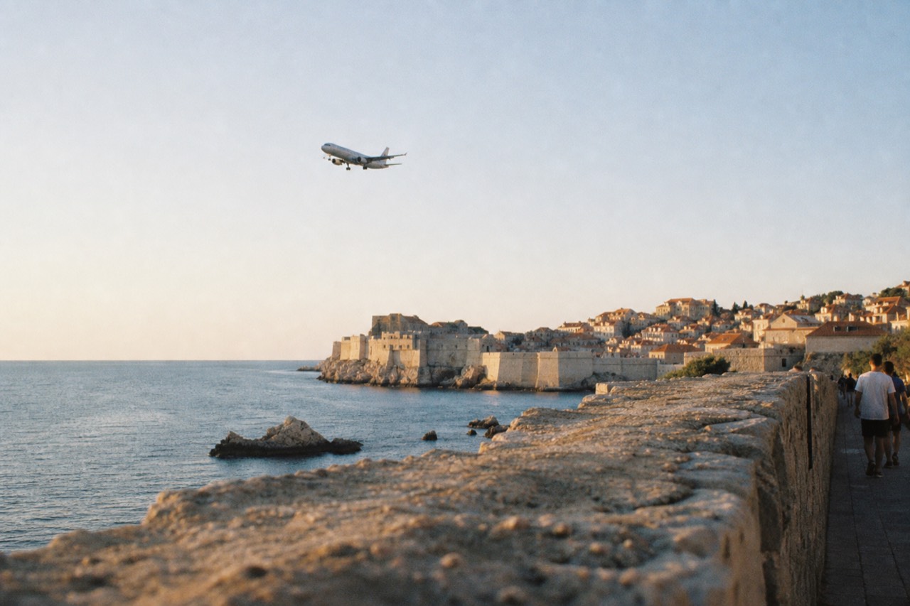 A plane descending over the Adriatic coast near Dubrovnik with red rooftops in the distance