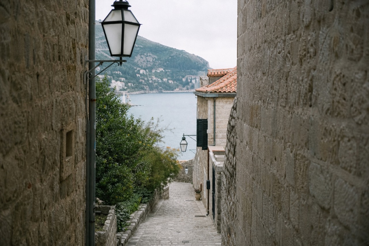 A quiet cobblestone alley in Dubrovnik with stone buildings and lanterns, no people.