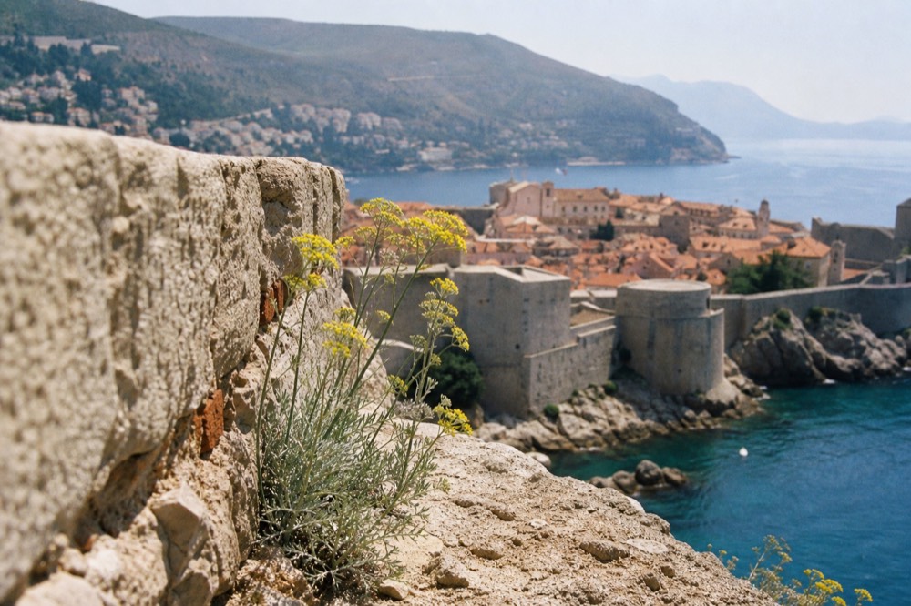 Medieval stone walls of Dubrovnik rising above red rooftops toward the sea