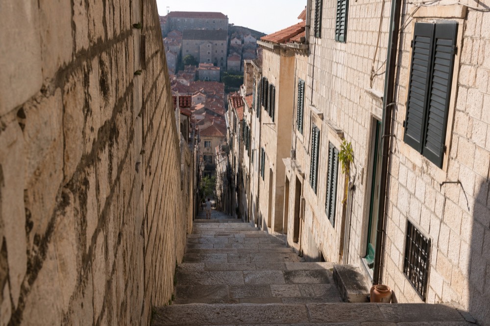 Stone staircase in Dubrovnik Old Town climbing between tall shuttered buildings in bright sunlight