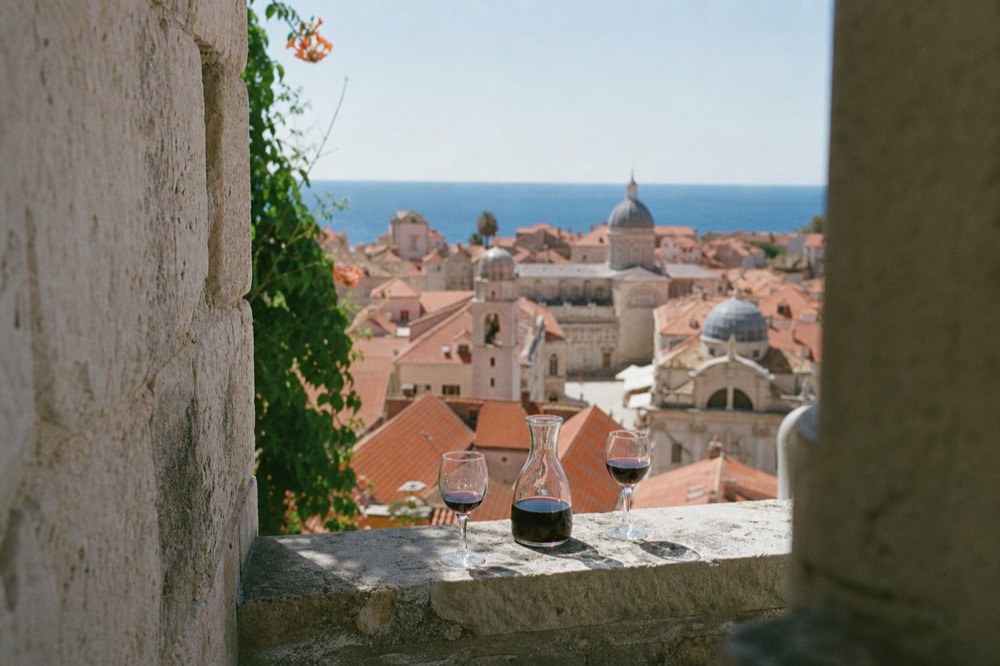 A carafe of local red wine and two glasses on a stone ledge overlooking Dubrovnik rooftops