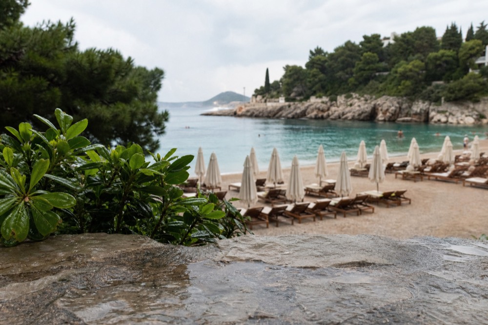 A wide bay beach with rows of sun loungers under parasols and calm turquoise water