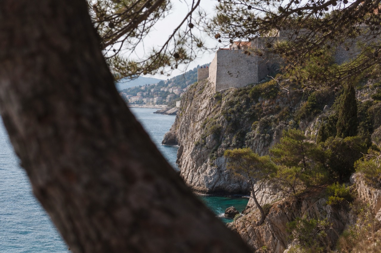 A stone cliff face below Dubrovnik's city walls dropping to clear blue Adriatic water