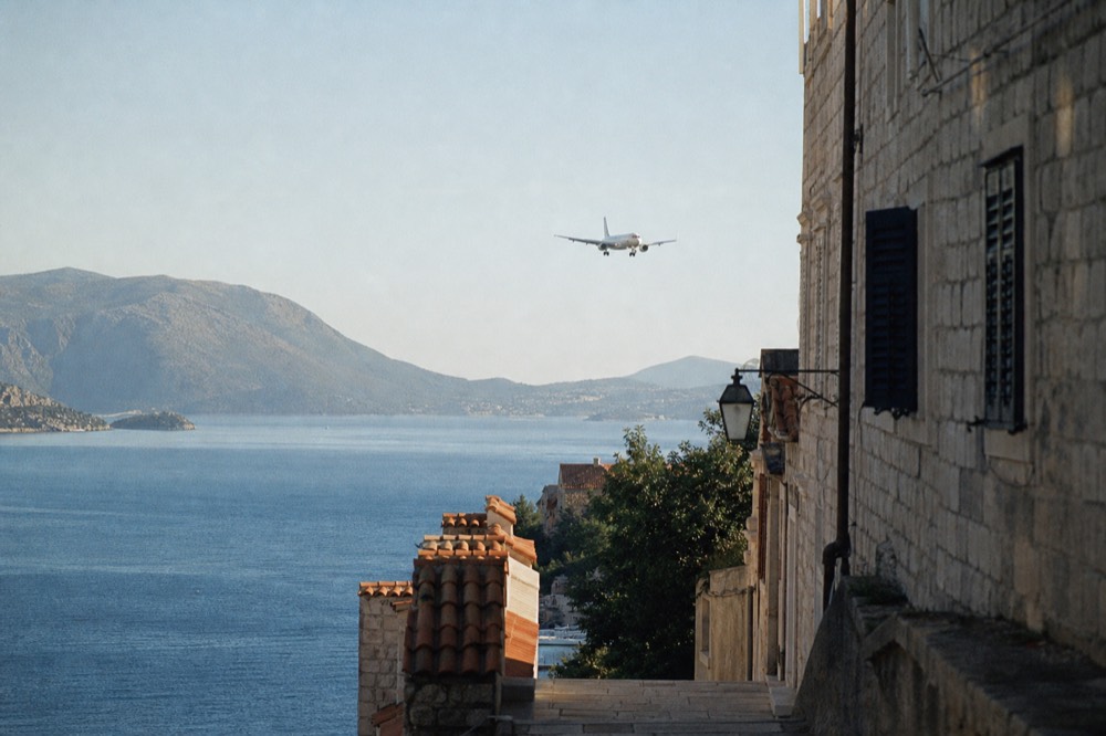 A plane descending over the Adriatic coastline toward Dubrovnik with rocky hills and blue sea below