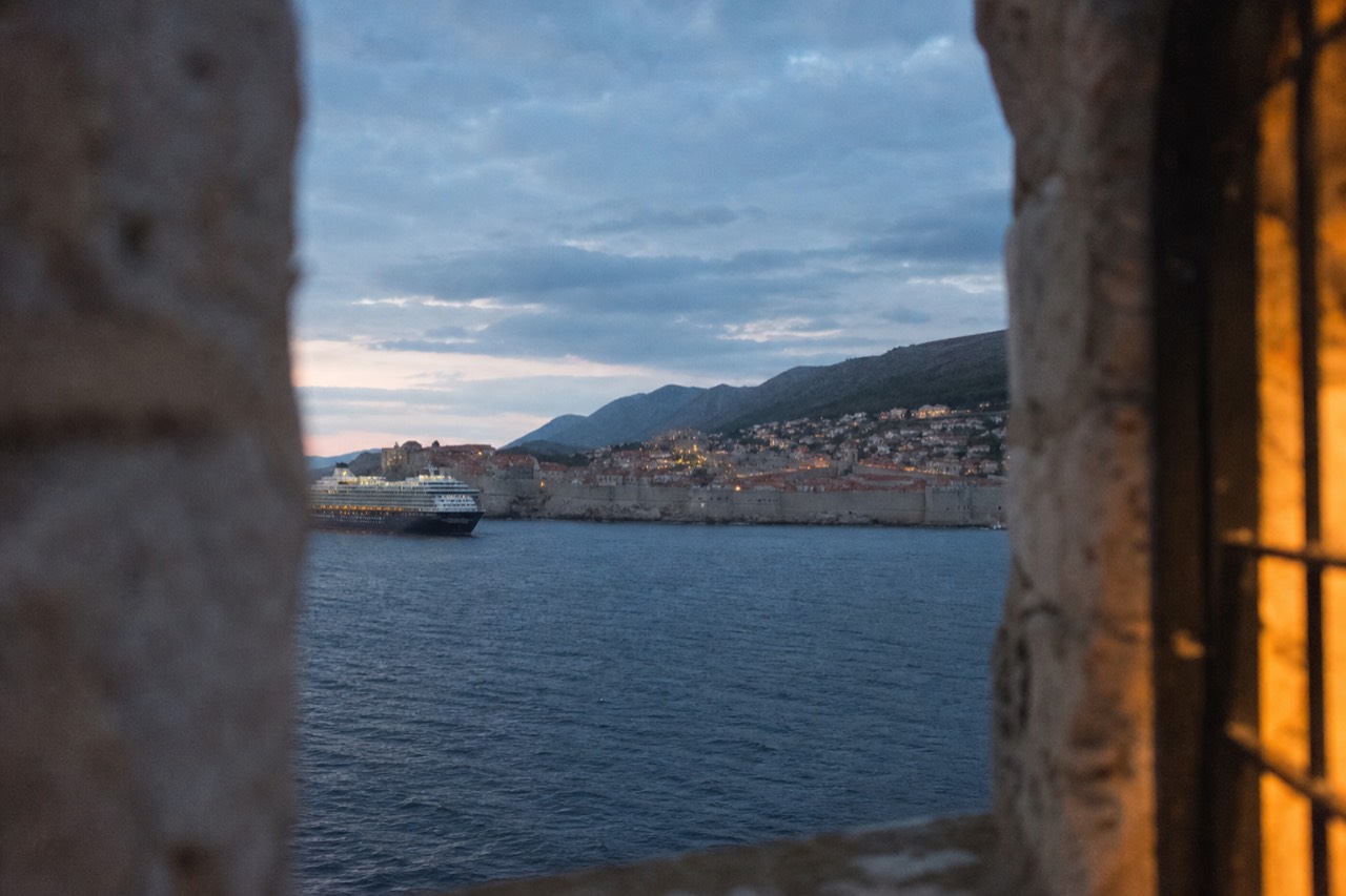 The walled Old Town of Dubrovnik seen from the sea with terracotta rooftops and a cruise ship anchored offshore