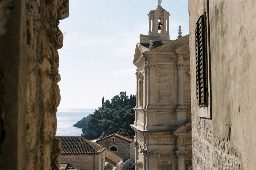 Sunlit stone facade of a Baroque church in Dubrovnik with shutters and a bell tower