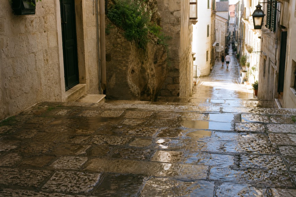 Rain-darkened limestone lane in Dubrovnik Old Town with wet stone steps glistening under evening light